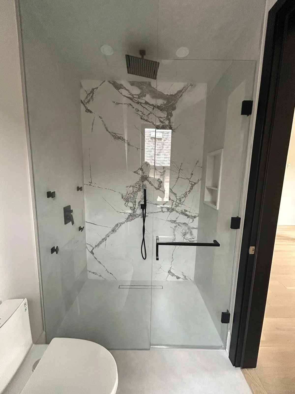 Walk-in shower finished in book-matched marble-effect porcelain with a frameless glass screen and linear drain