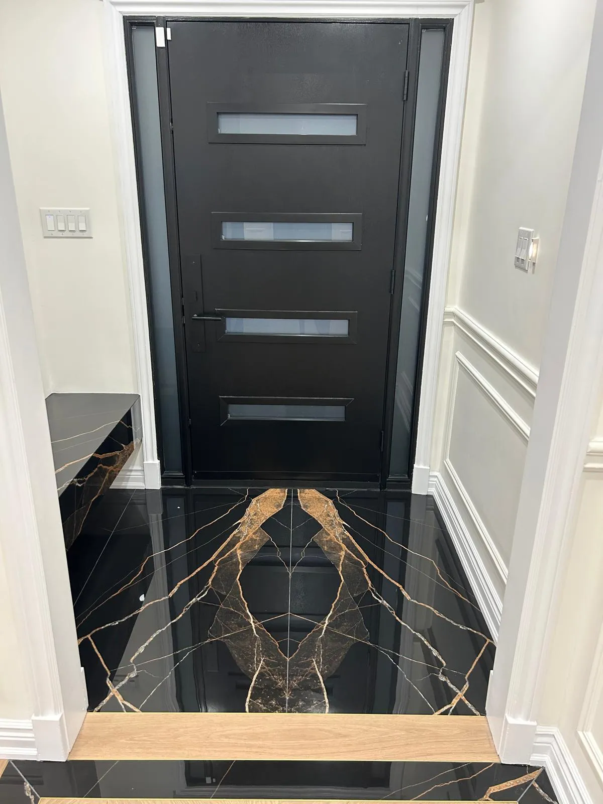 Entry hall with book-matched black and gold marble-effect porcelain flooring and a modern black entry door