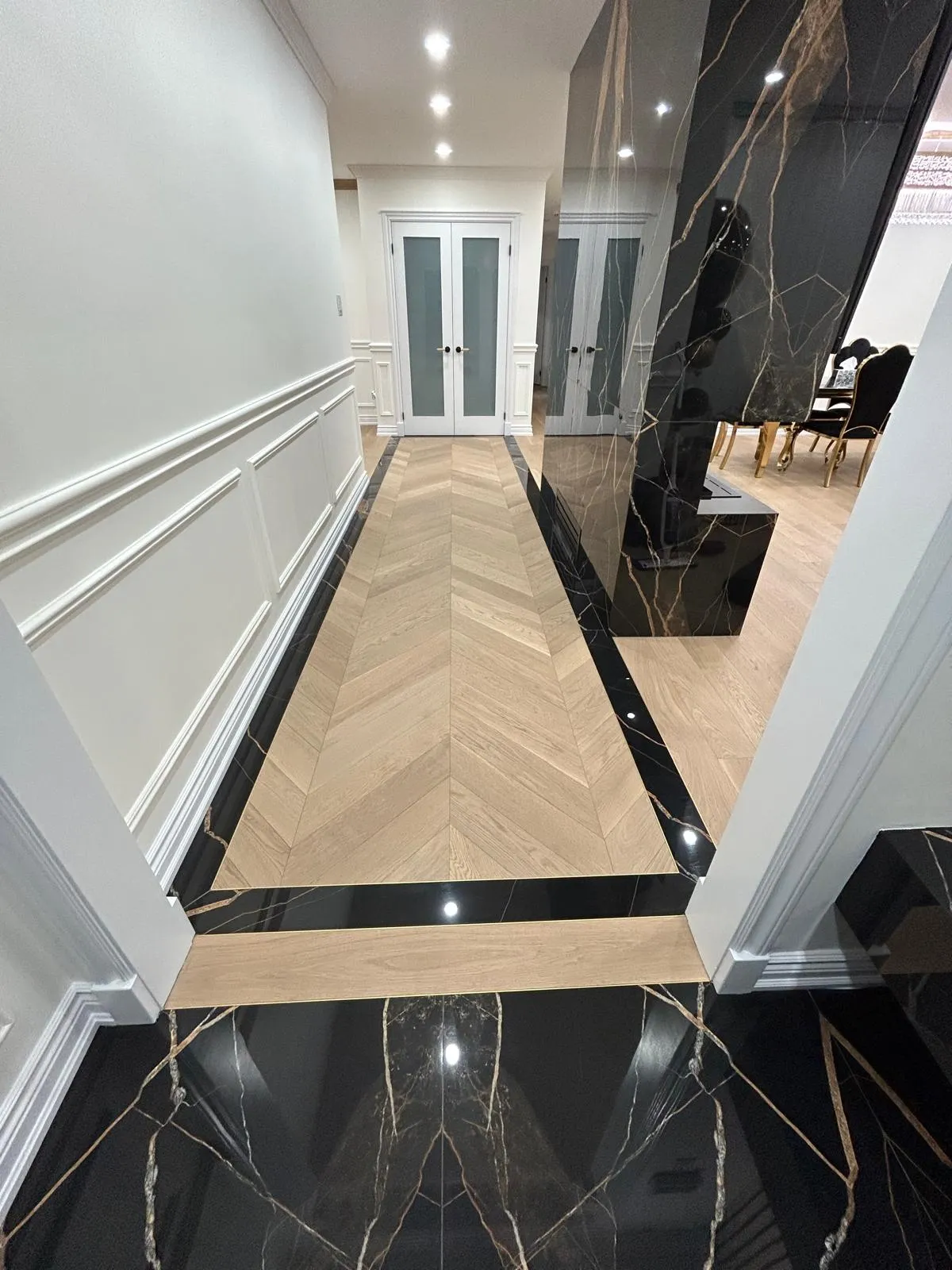 Chevron engineered oak flooring with a black marble inlay border, running into a custom millwork kitchen
