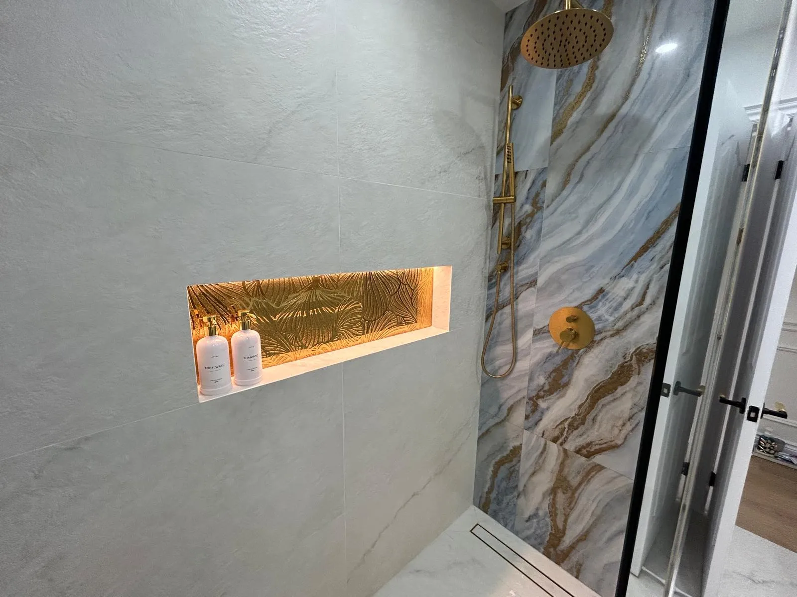 Curbless walk-in shower with a blue onyx feature panel, brass fixtures and a backlit recessed niche