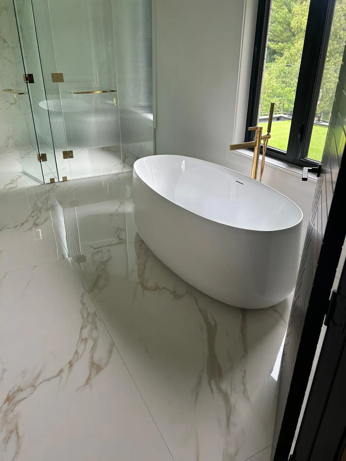Freestanding soaker tub on book-matched Calacatta-effect porcelain with a floor-mounted brass filler, master ensuite in Whitby