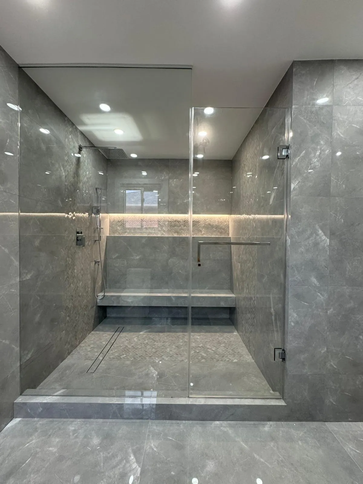 Large grey marble-effect steam shower with a built-in bench, linear drain and frameless glass