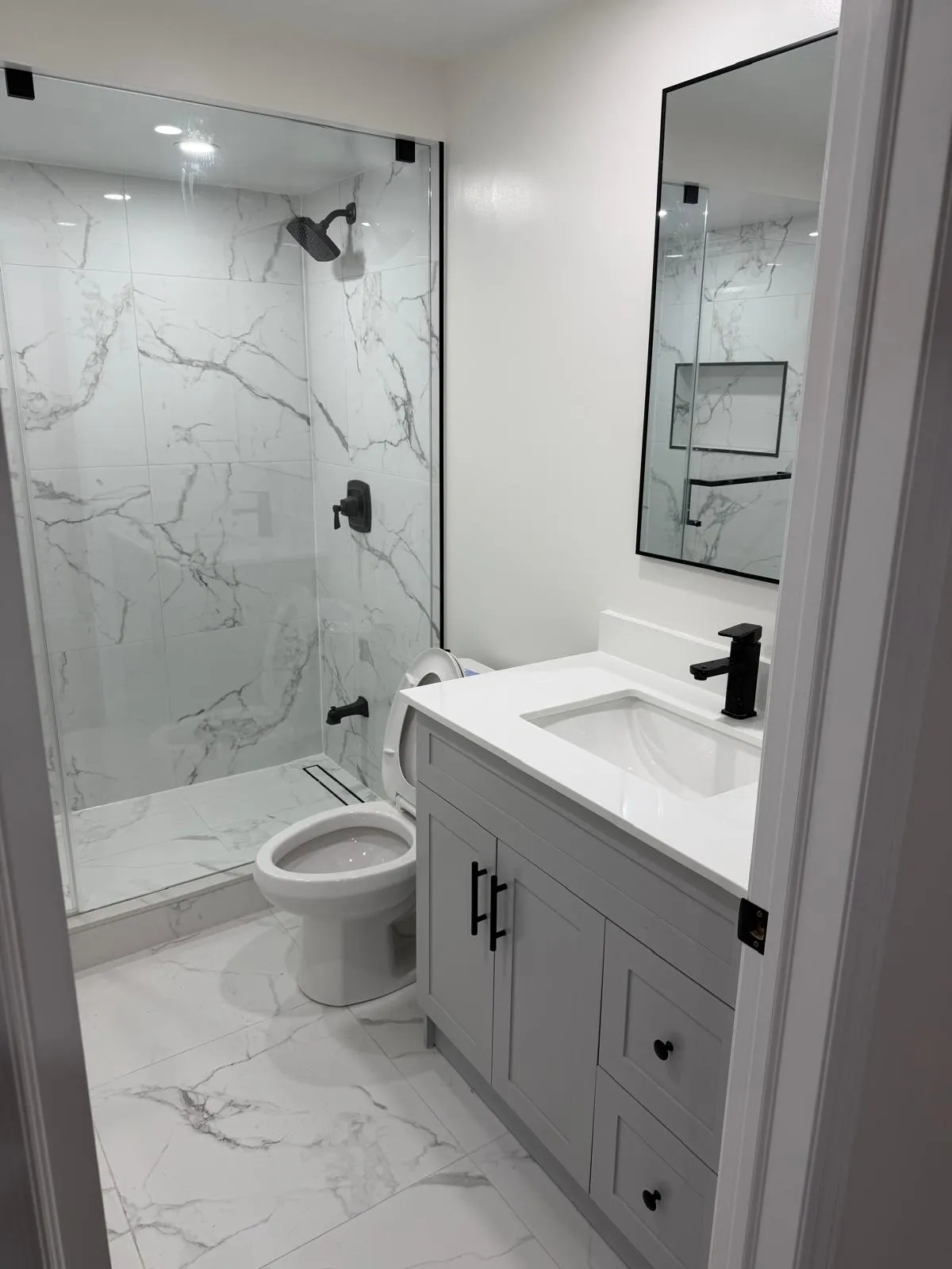Walk-in shower in grey marble-effect porcelain with a full-width bench and frameless glass door