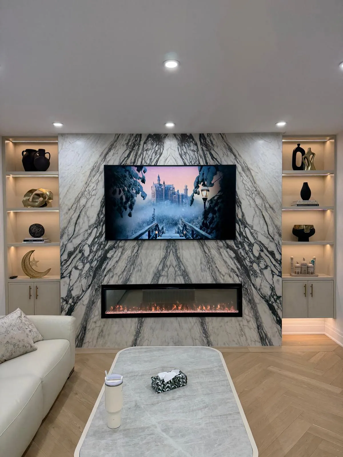 Living room feature wall in book-matched marble-effect porcelain with a linear fireplace and lit shelving
